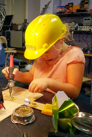 Girl soldering while wearing a hard hat