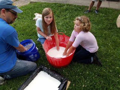 Instructor and kids mixing oobleck outdoors on the grass