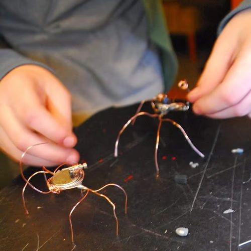 Child's hands assembling a bug bot from electronic components and copper wire legs