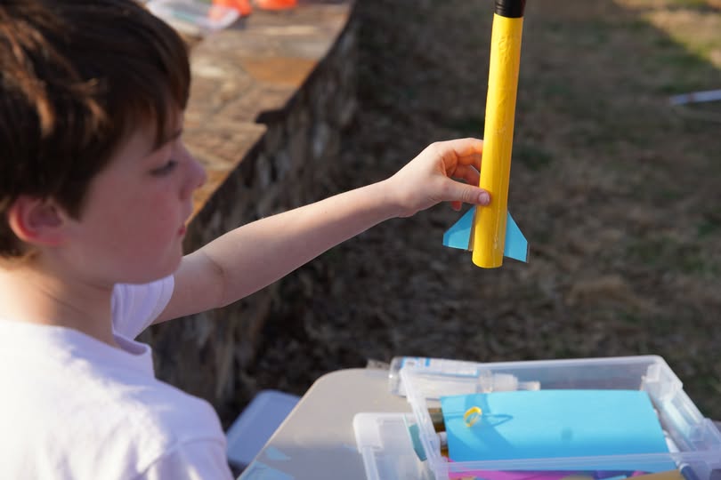 Boy proudly inspecting his handmade yellow compressed air rocket with blue fins