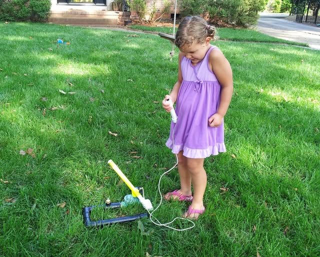 Young girl in a purple dress standing at the compressed air rocket launcher in a sunny yard