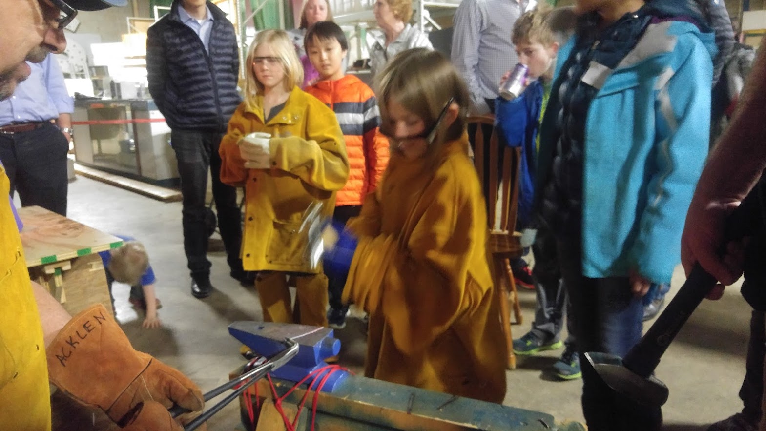 Kids in safety gear at blacksmithing workshop with anvil