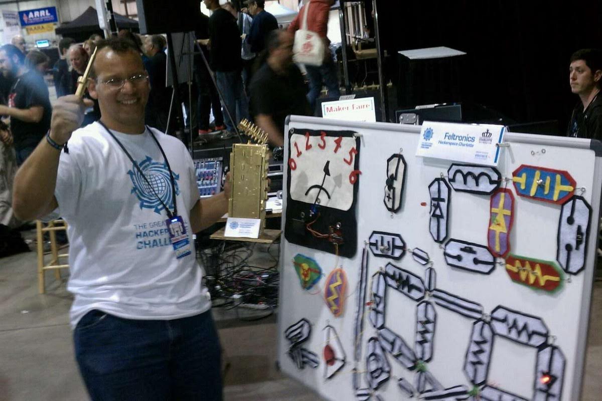Quincy at Maker Faire wearing a Great Global Hackerspace Challenge shirt, holding the winning trophy next to his Feltronics educational electronics display