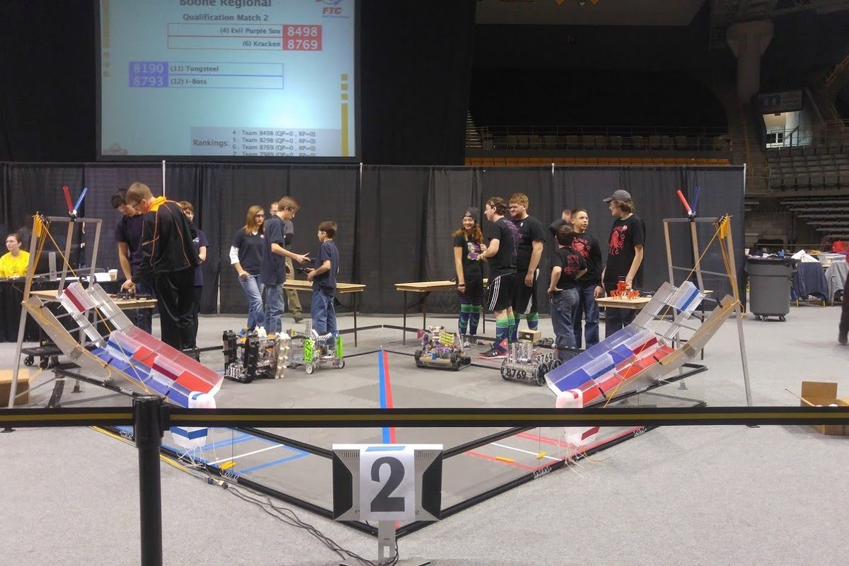 FIRST Tech Challenge robotics competition with student teams operating their robots on a large arena field while spectators watch from the sidelines