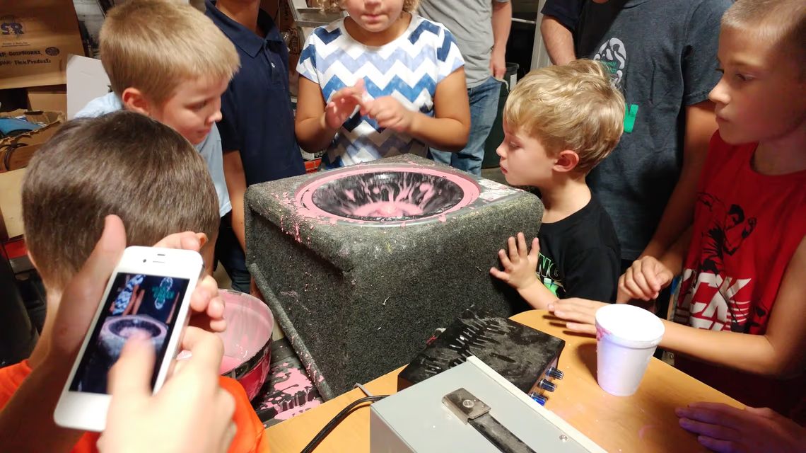 Kids gathered around a speaker watching oobleck dance to bass frequencies