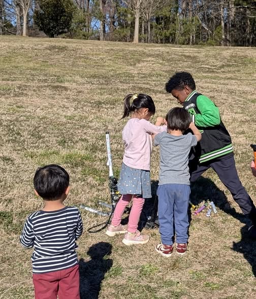 Group of young kids eagerly crowding around the compressed air rocket launcher