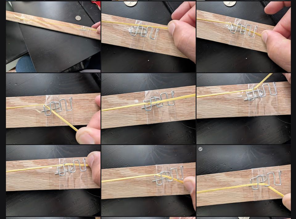 Rubber band threaded through the paper clip descender on the wooden test rig, showing the weaving pattern